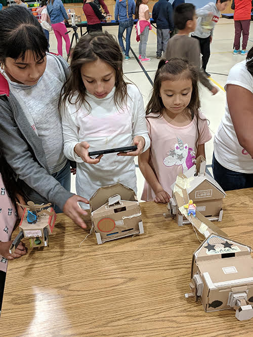 students using handheld computer to activate cardboard toys 