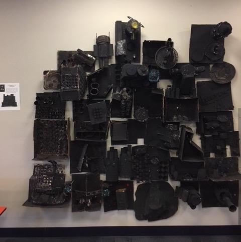 This image shows a variety of recycled, 3D objects hot glued together and spray-painted black, to create a large installation.